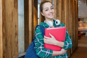 Smiling student holding books and wearing headphones, representing success and readiness for study abroad with My School Abroad consultancy