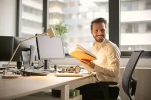 Smiling professional holding a book at his desk in a modern office