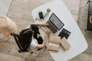 Top view of a woman using a desktop computer and studying with books on a table